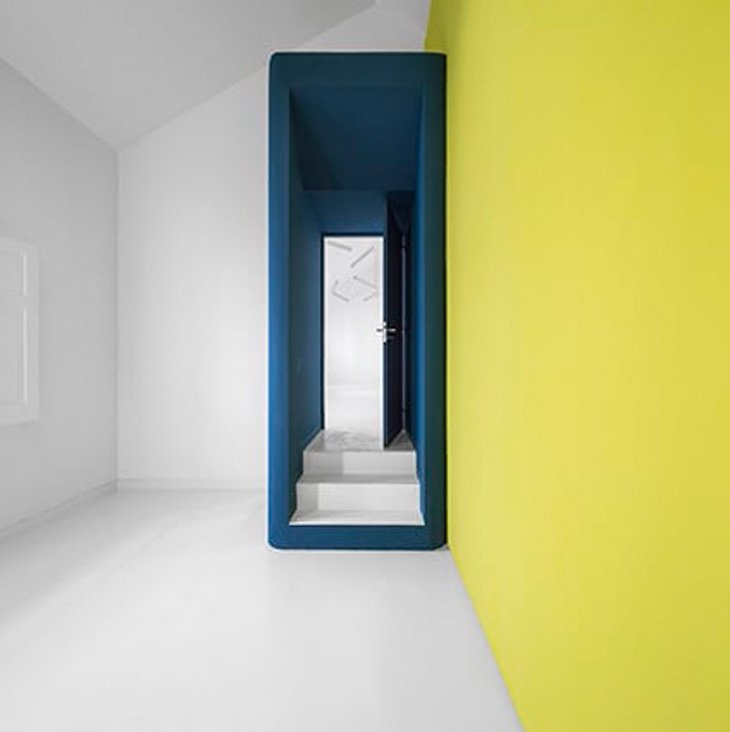 Vista estancia interior con pared amarilla y pasillo azul en Transforma Estudios